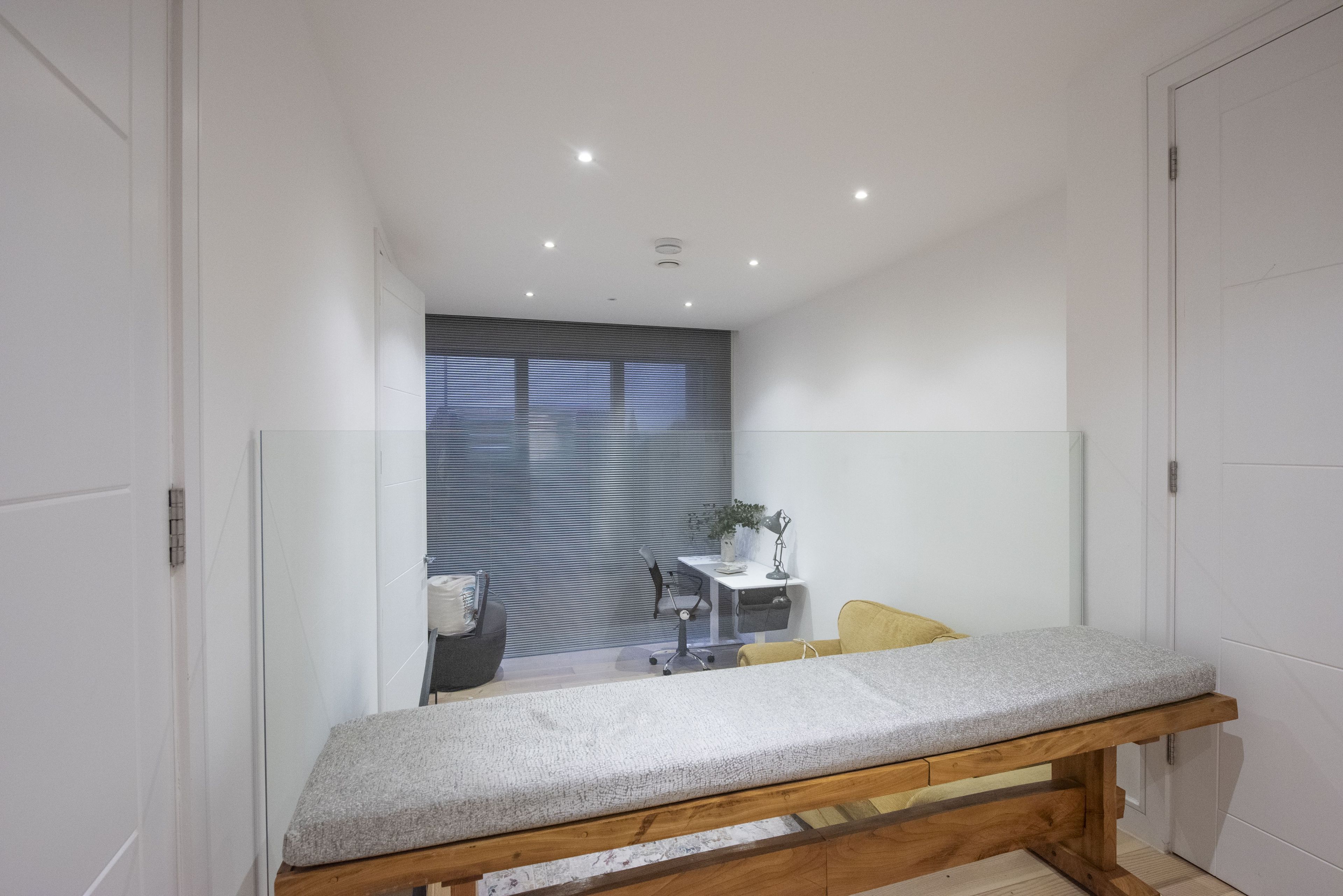 A modern, well-lit room with a wooden bench, a small desk with a chair, and a window with blinds.
