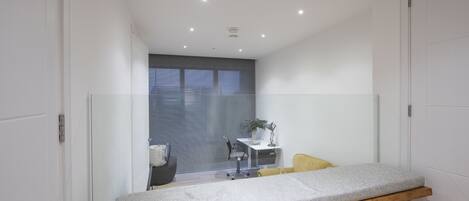 A modern, well-lit room with a wooden bench, a small desk with a chair, and a window with blinds.