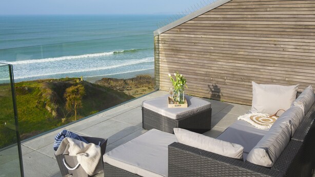 A balcony with a view of the ocean, wicker furniture, and a glass barrier. - At 1 Island Reach, you'll find yourself just steps away from pristine beaches (Newquay)