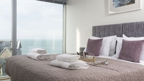 A hotel room with a large bed, a view of the sea, and a framed picture on the wall. - At 1 Island Reach, you'll find yourself just steps away from pristine beaches (Newquay)