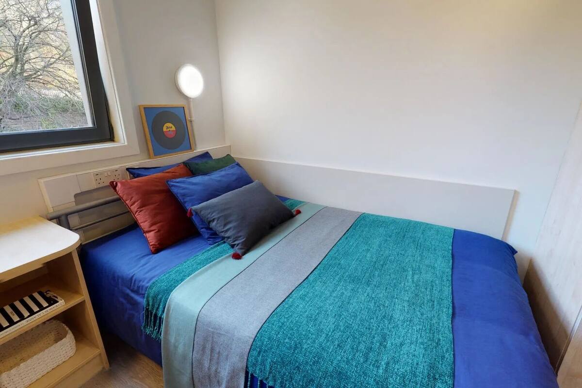 A bedroom with a bed, a window, a bedside table, and a shelf.