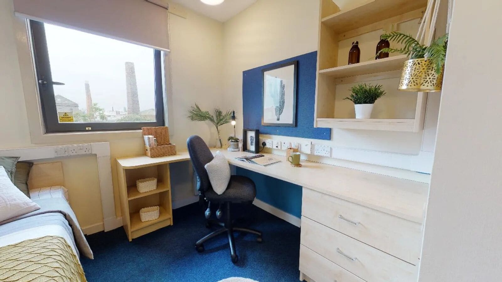 A compact bedroom with a bed, a desk, and a chair. There is a window with a view of buildings outside.