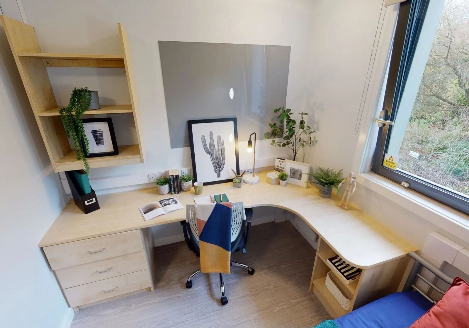 A modern workspace with a curved desk, a chair, a bookshelf, and a window with a view of trees.