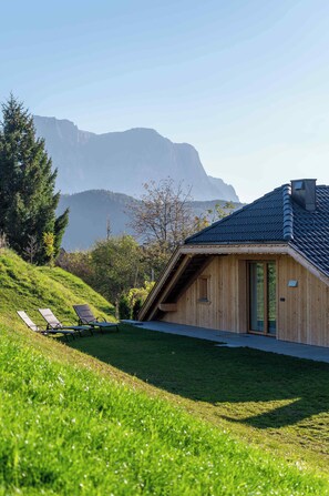 A wooden cabin with a sloped roof, a grassy lawn, and a mountain backdrop. - Chalet Roderer (Lajen)