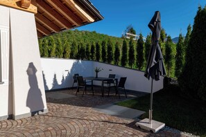 Un patio con una mesa y sillas, una pérgola y vistas a una ladera boscosa.