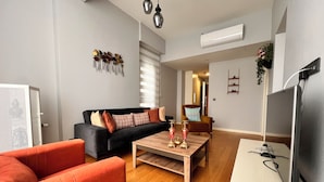 A living room with a black sofa, orange armchairs, a wooden coffee table, and a TV. - G Tower Residence Apartment Rentals (Istanbul)