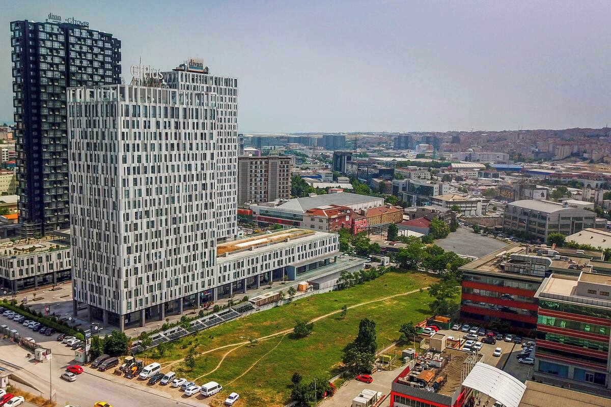 Un immeuble de grande hauteur à la façade structurée en forme de grille, entouré d’autres bâtiments et d’un parking.