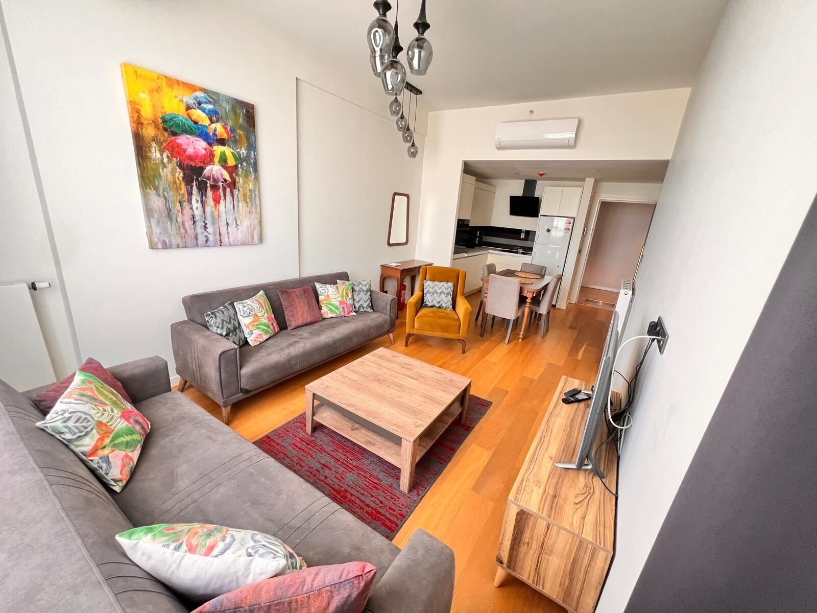 Ein modernes Wohnzimmer mit einem grauen Sofa, einem Holztisch und einem farbenfrohen Bild an der Wand.
