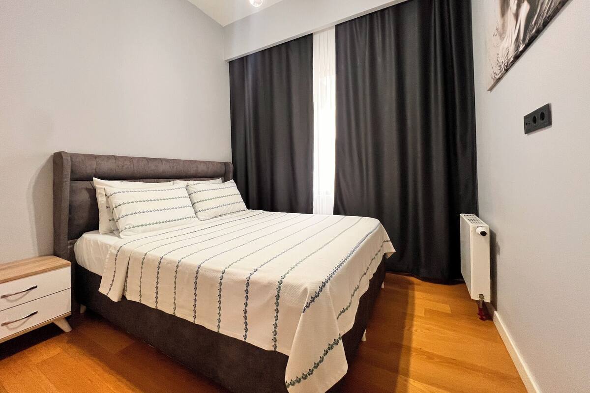 Une chambre à coucher avec un lit, des tables de chevet, un radiateur et une fenêtre avec des rideaux.