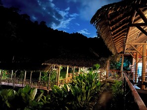 A thatched-roof structure with a wooden deck and surrounding lush greenery. - Rafiki Safari Lodge (Río Nuevo)