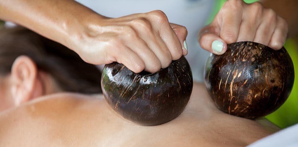 Eine Massageanwendung: Eine Person erhält eine Kopfmassage mit einem Stein.