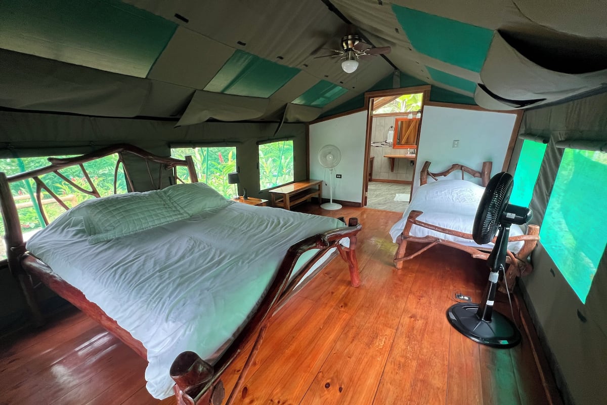 Una habitación amplia con una cama grande, una silla de madera y un ventilador de techo.