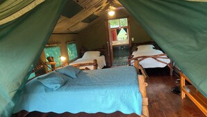 A cozy tented accommodation with two wooden beds, a small bathroom, and a view of the outdoors. - Rafiki Safari Lodge (Río Nuevo)
