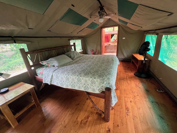 A tented accommodation with a wooden bed, a desk, and a chair. - Rafiki Safari Lodge (Río Nuevo)
