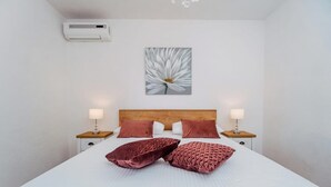 A hotel room with a large bed, two bedside lamps, a wall-mounted air conditioner, and a floral artwork above the bed. - New! Studio partment A1 in Okrug Donji (Okrug Donji)