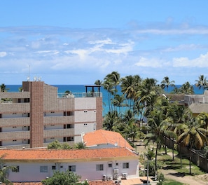 Ein mehrstöckiges Gebäude mit Balkonen, die auf einen Strand, Palmen und einen strahlend blauen Himmel blicken.