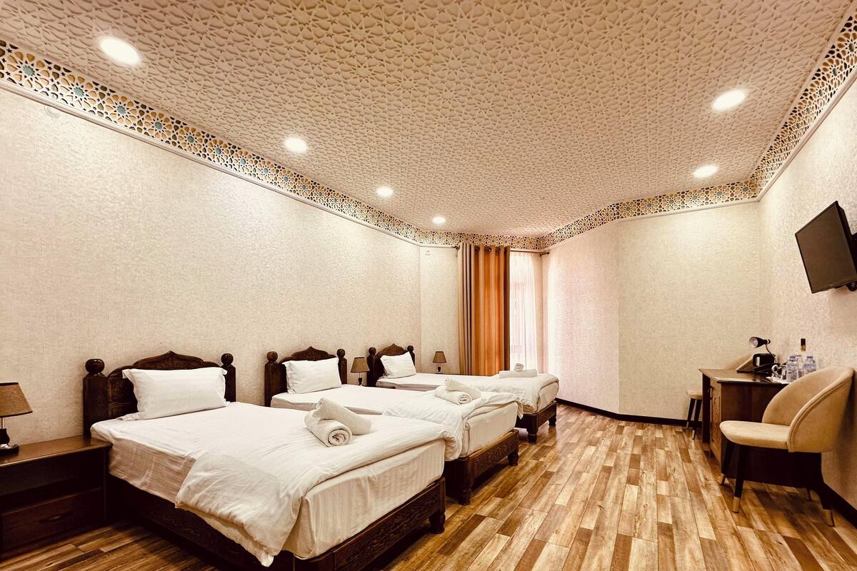 A hotel room with three beds, wooden flooring, a flat-screen TV, and a desk with a chair.