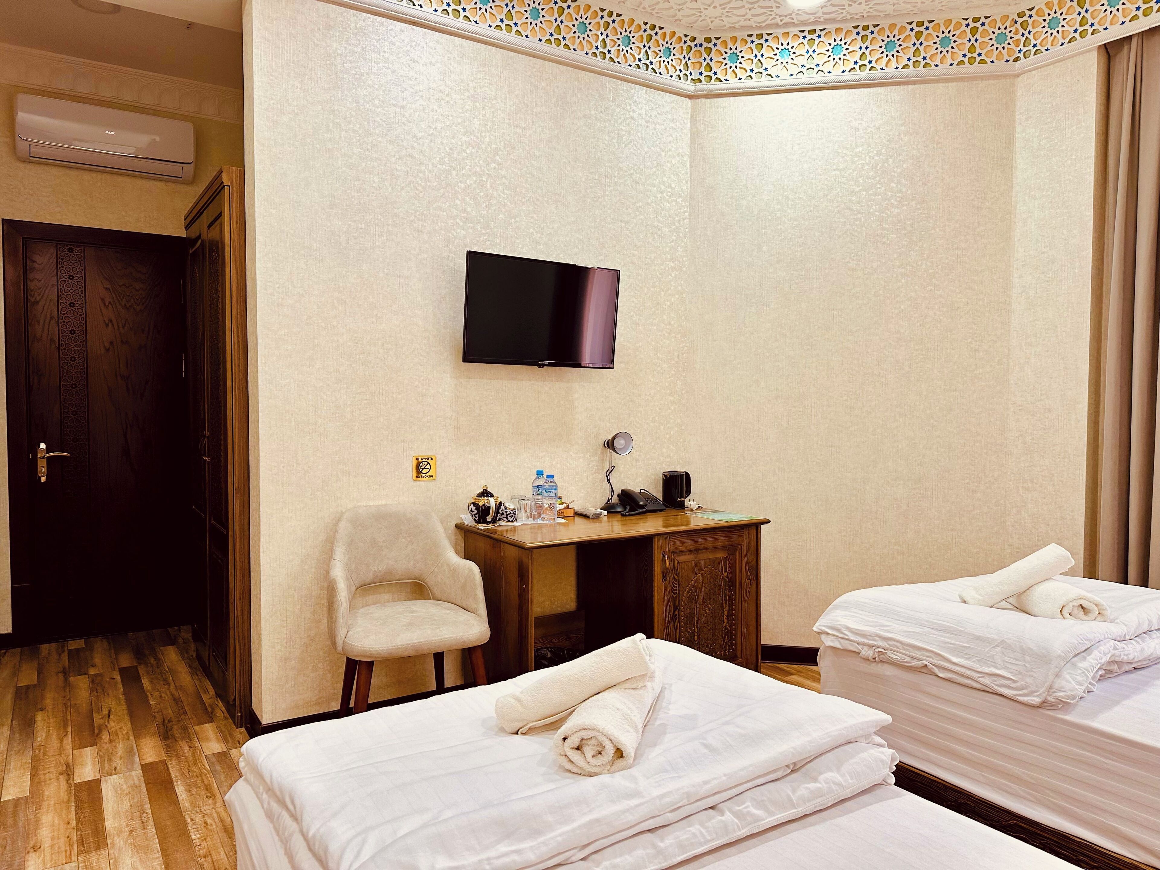 A hotel room with a bed, a desk with a chair, a flat-screen TV, and an air conditioning unit.