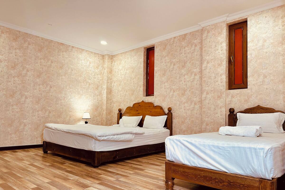 A hotel room with two wooden beds, a wooden floor, and patterned wallpaper.