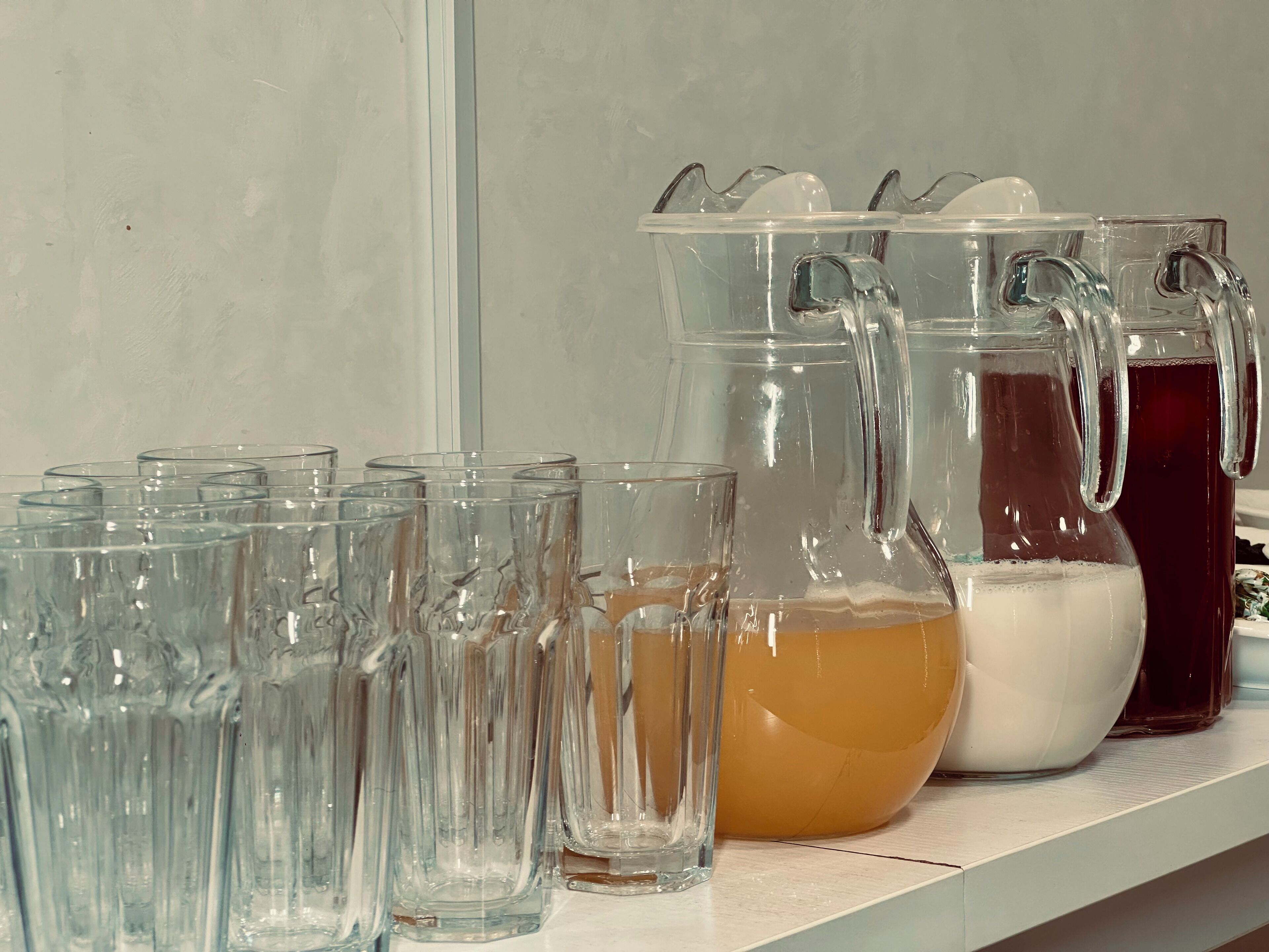 Una colección de vasos y jarras de vidrio transparente con diferentes líquidos sobre una estantería.