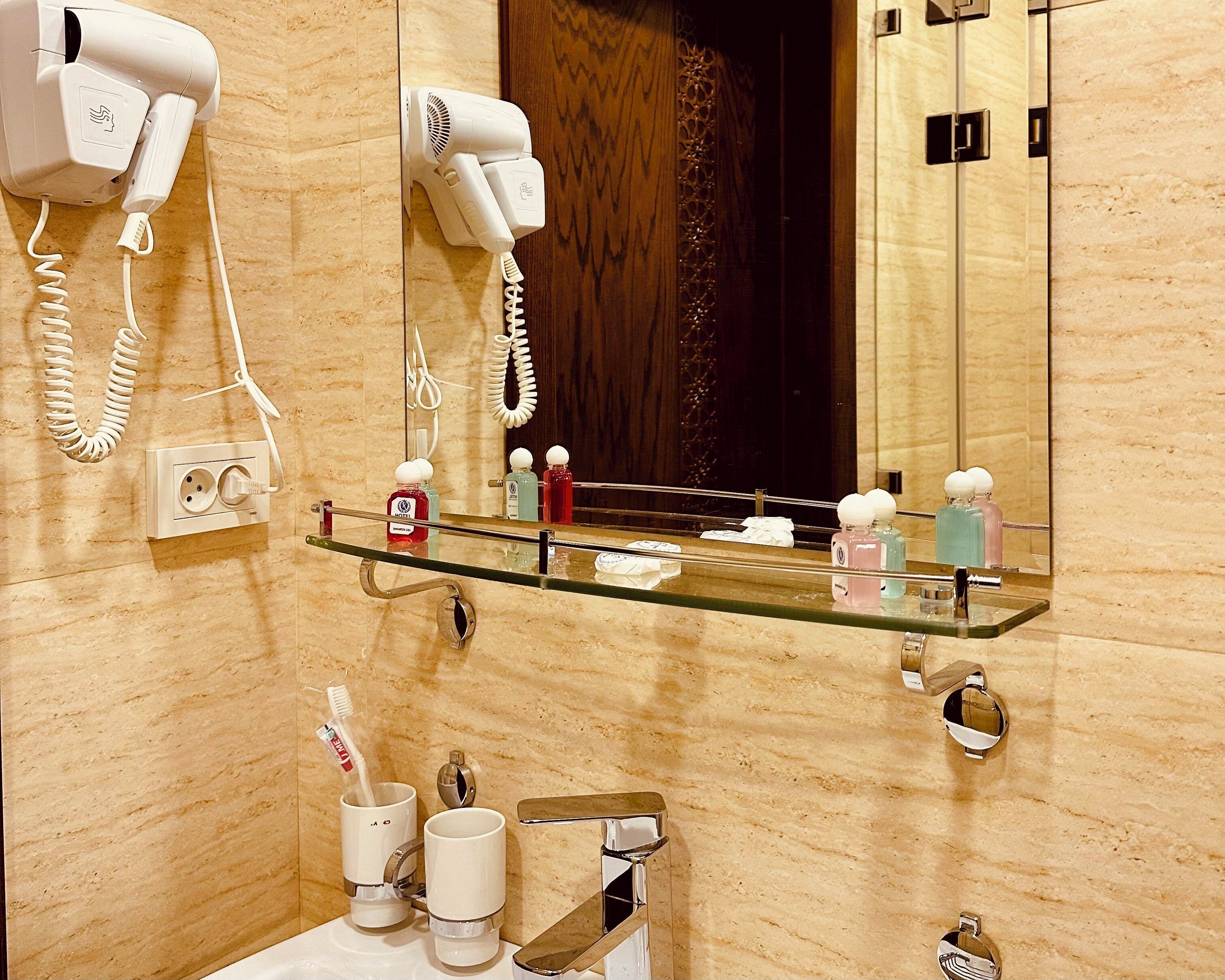 A bathroom with a glass shelf holding toiletries, a hairdryer, and a telephone.