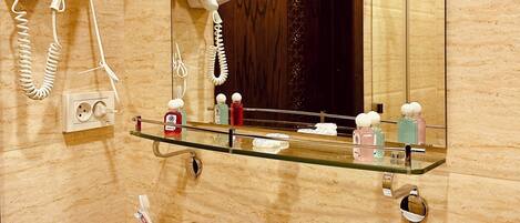 A bathroom with a glass shelf holding toiletries, a hairdryer, and a telephone.