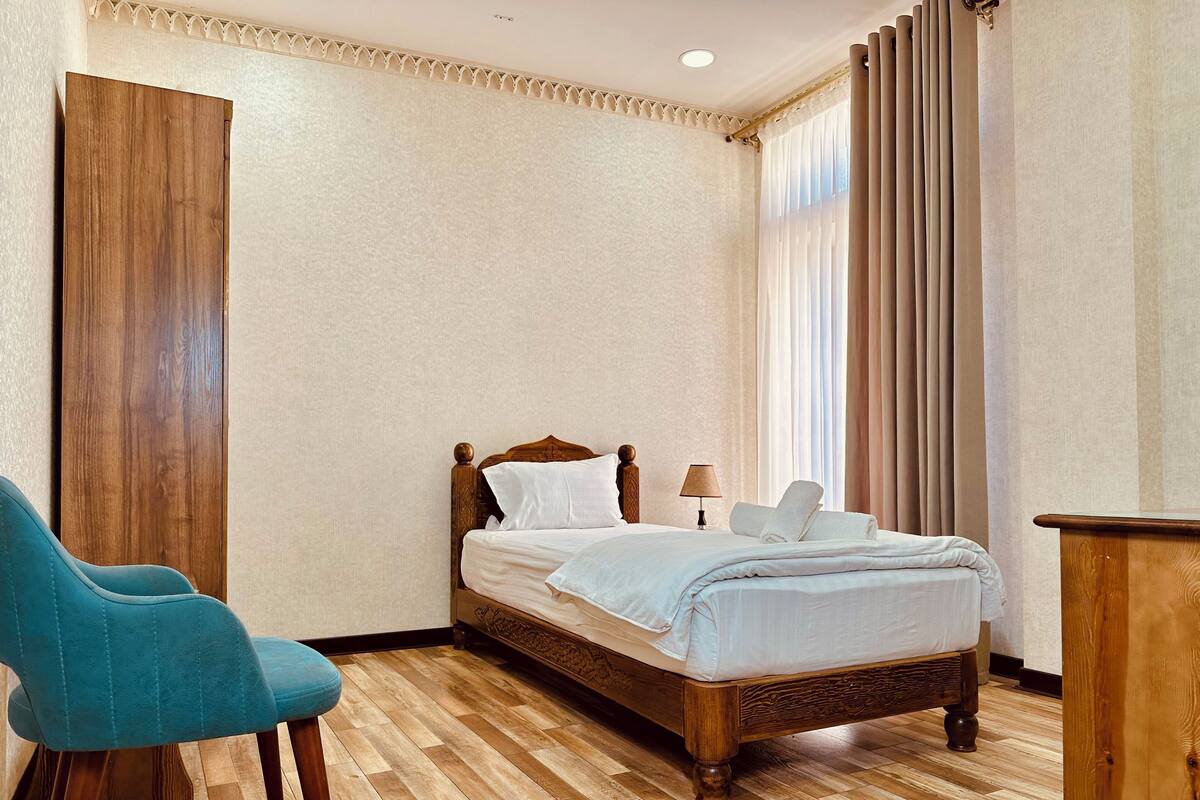 A neatly arranged bedroom with a wooden bed, a blue chair, and a wooden desk.