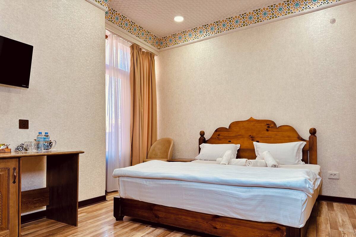 A neatly arranged hotel room with a wooden bed, a small desk, and a television mounted on the wall.