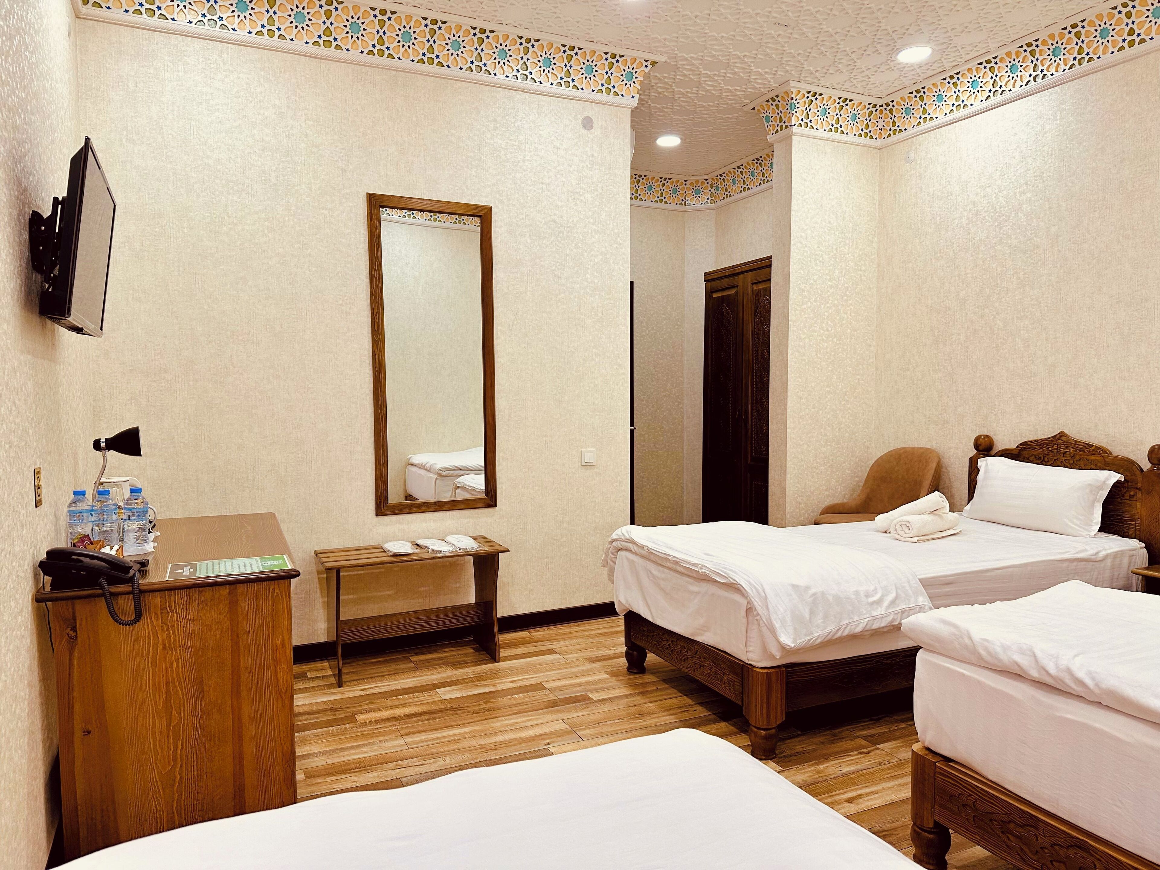 A hotel room with two beds, a wooden desk, a mirror, and a television.