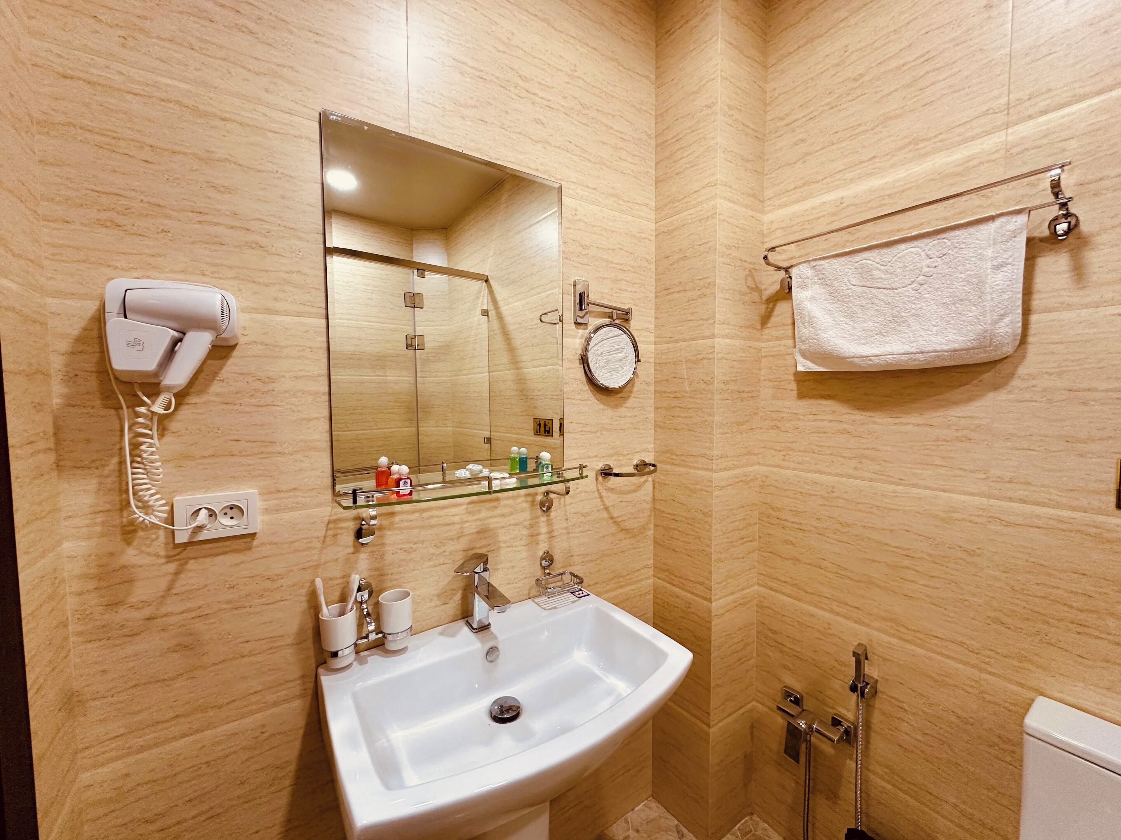 Une salle de bain avec un lavabo blanc, un sèche-cheveux, un miroir et un porte-serviettes.