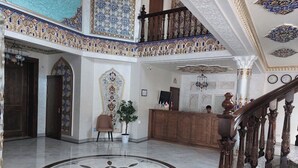 Un amplio vestíbulo con piso de mármol, decoraciones ornamentales en las paredes y una escalera de madera.