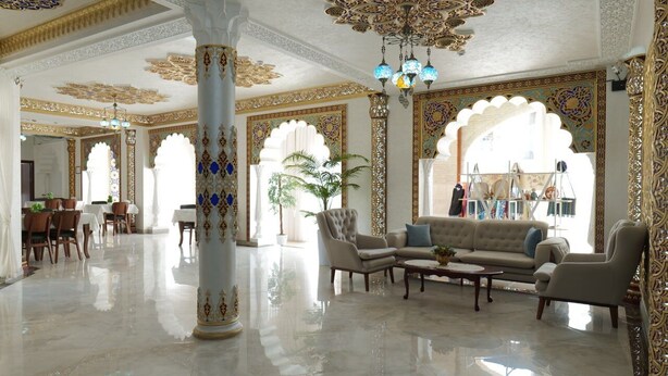 Un vestíbulo amplio con columnas ornamentales, una zona de estar con sofás y sillones, y un comedor con mesas y sillas.