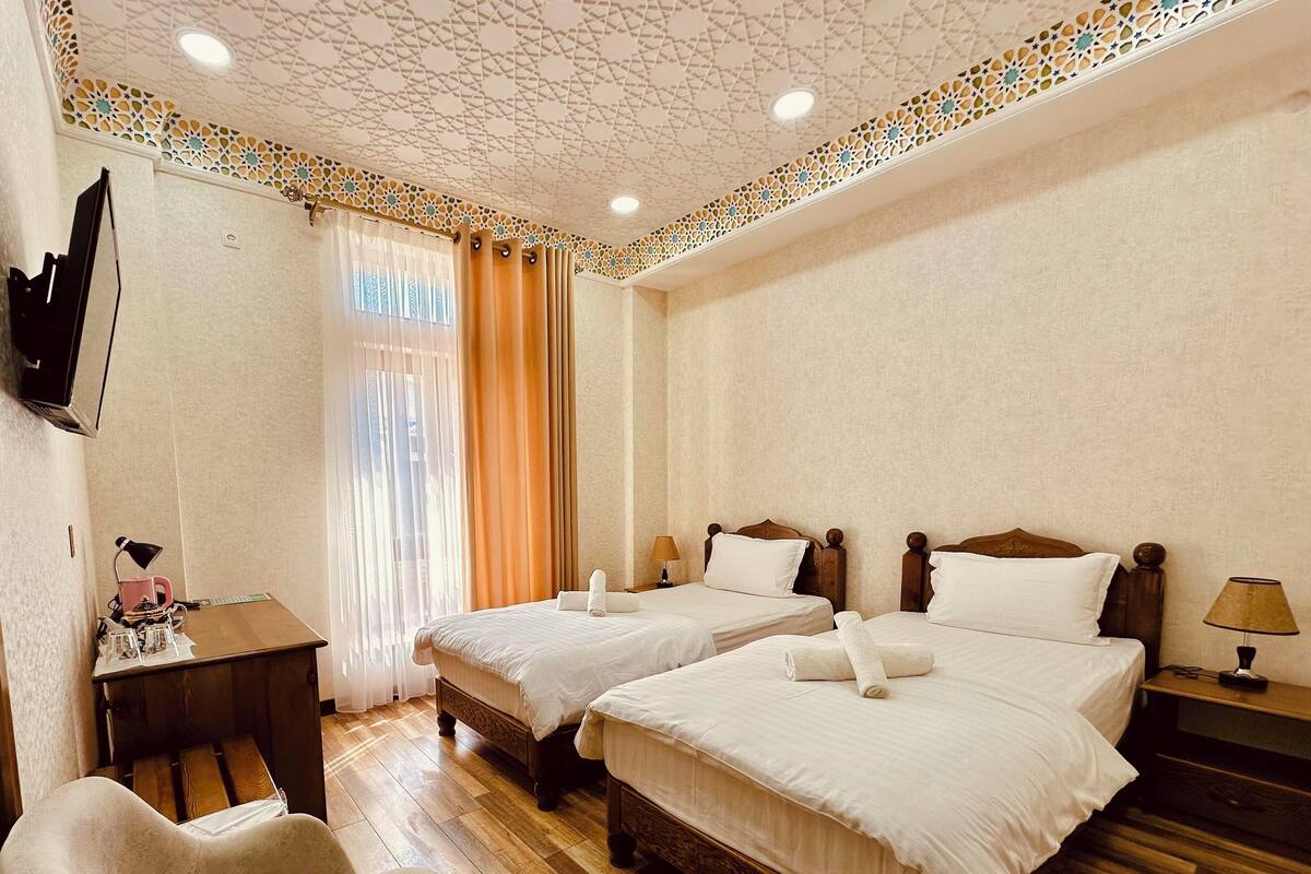 A hotel room with two beds, a desk, a chair, and a TV mounted on the wall.