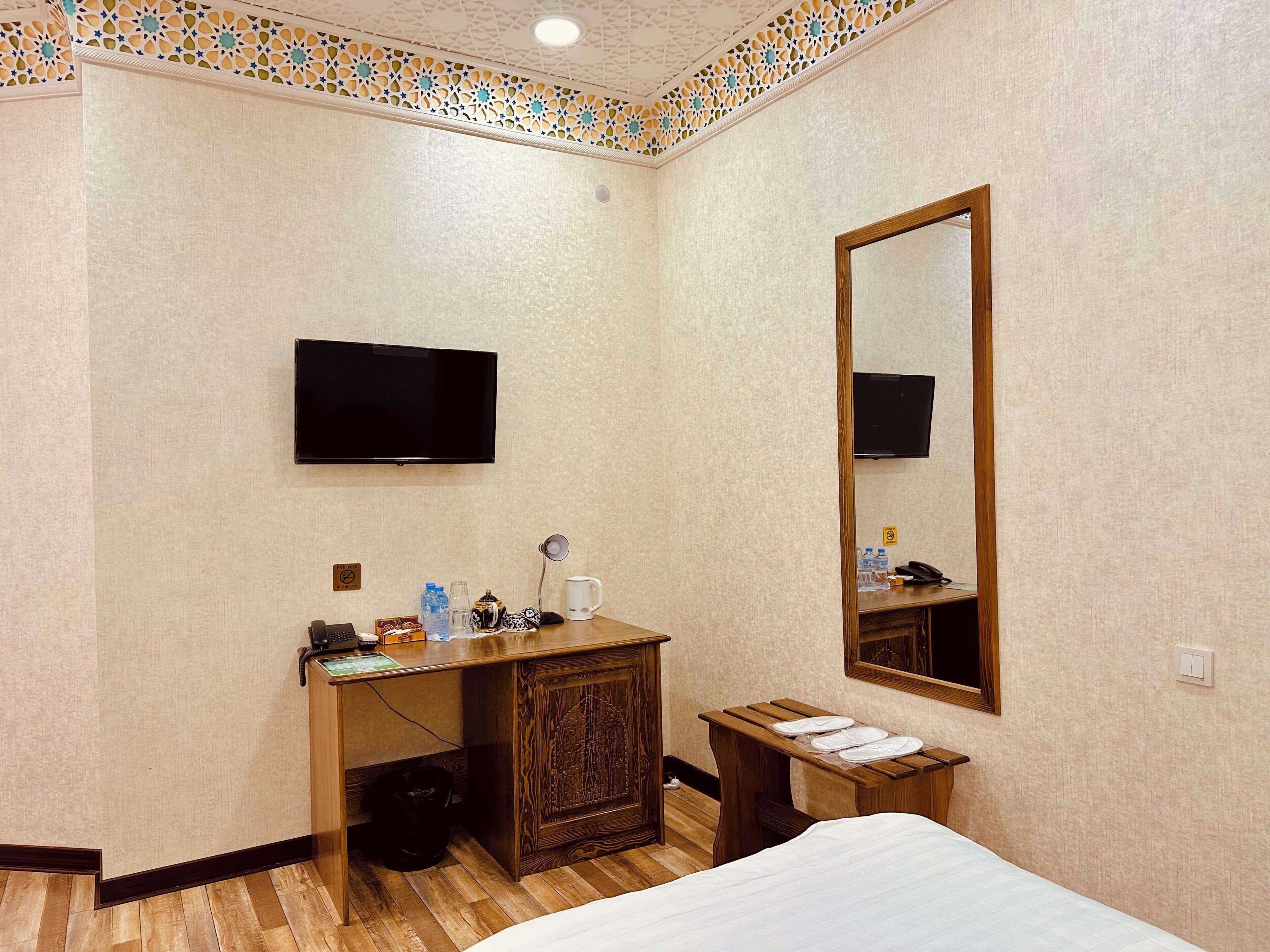Una habitación de hotel con una cama, un escritorio con teléfono, un espejo y un televisor fijado a la pared.