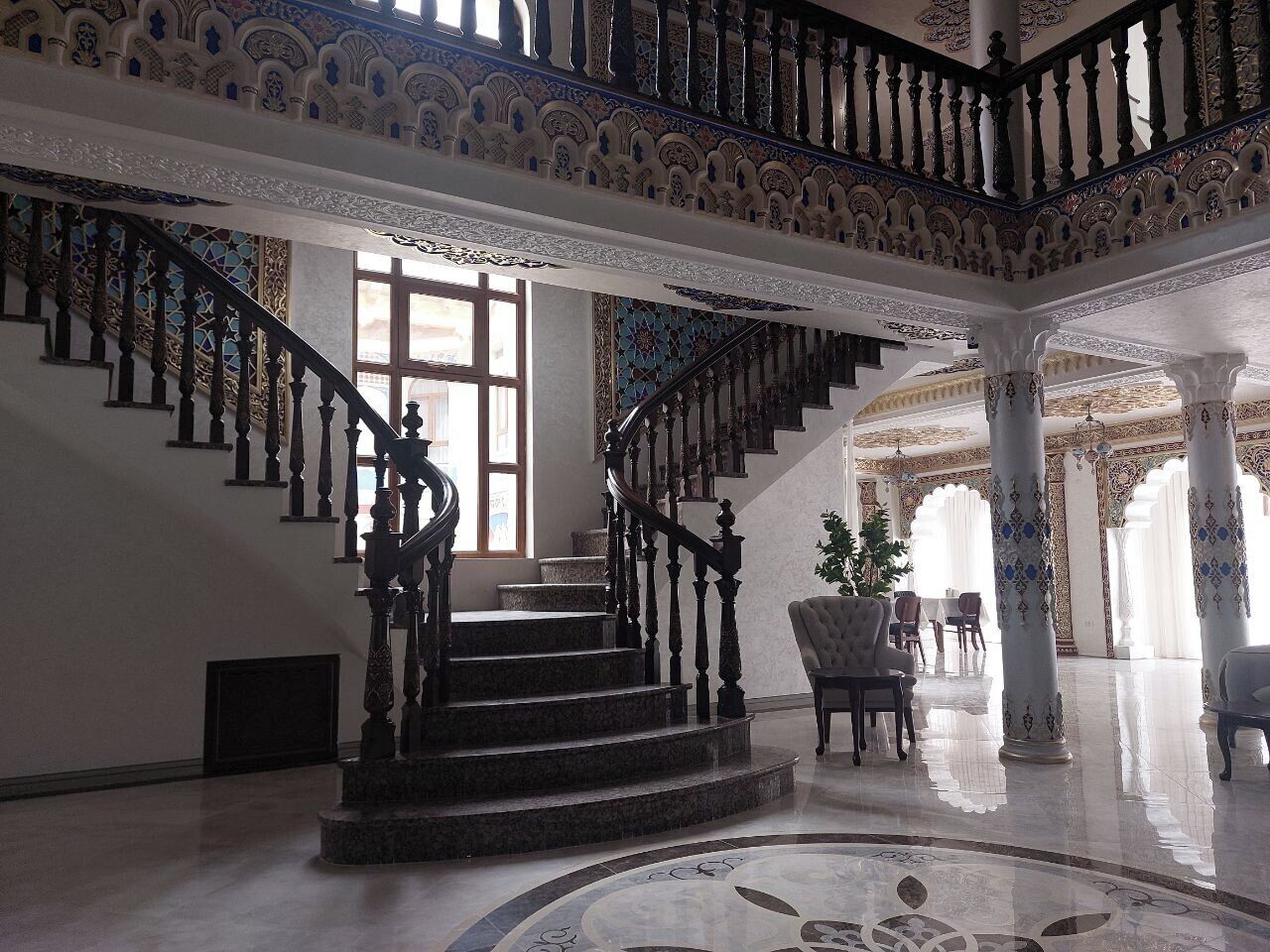 A grand staircase with ornate railings, leading to a spacious lobby with high ceilings and decorative columns.