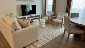 A living room with a sofa, two armchairs, a coffee table, and a TV on a white stand.