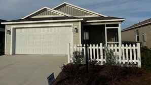 A single-story house with a garage, a covered entryway, and a white picket fence.