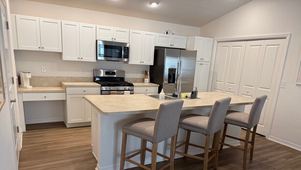A modern kitchen with white cabinets, stainless steel appliances, a wooden island with bar stools, and a wooden floor.
