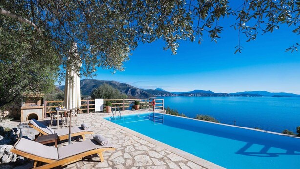 Ein Poolbereich mit Liegestühlen, einer Terrasse mit Steinplatten und Blick auf einen See und Berge.