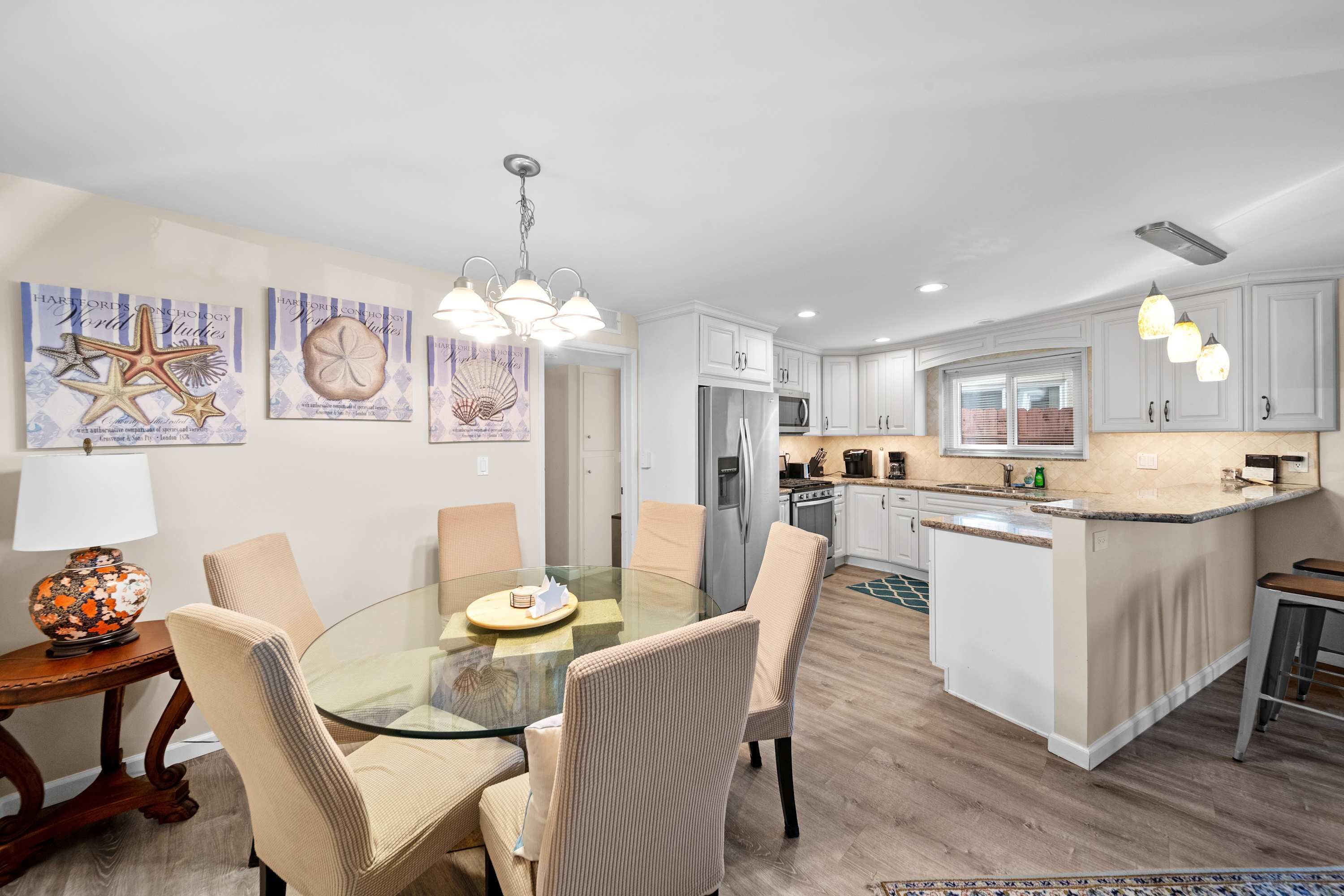 A modern kitchen with white cabinets, a central island, and a dining area with a glass table and cushioned chairs.