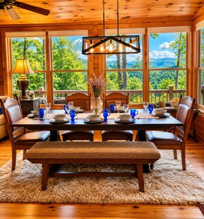 Un comedor de madera con una mesa dispuesta para seis, ventanas amplias y vistas a árboles y montañas.