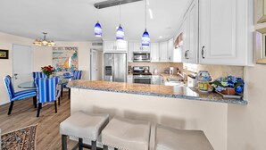 A modern kitchen with white cabinets, a granite countertop, and blue-striped chairs. - Ruby Villa B - Upper Unit for 6! (Newport Beach)