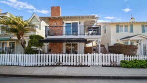 A two-story house with a balcony, a white picket fence, and a brick chimney. - Ruby Villa B - Upper Unit for 6! (Newport Beach)