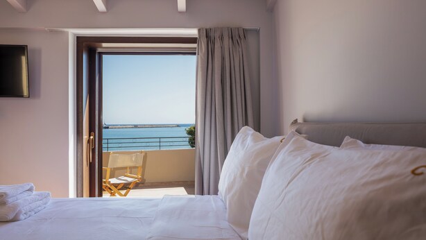 A hotel room with a bed, a balcony with a view of the sea, and a chair. - Chryssi 03, seafront cozy suite for 2 in Rethymno! (Rethymno)