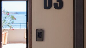 A door with the number 03, a keypad, and a view of the sea through an open door. - Chryssi 03, seafront cozy suite for 2 in Rethymno! (Rethymno)