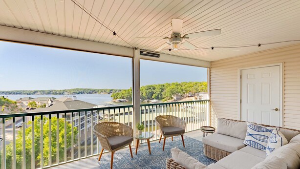 A balcony with wicker furniture, a ceiling fan, and a view of a river and buildings. - Highland Shores Haven Fit For 7 (Lake Ozark)