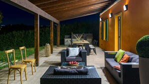 An outdoor patio area with seating arrangements, including chairs and sofas, and a table with a basket of fruit. - Villa Traiani 8&2 by Marche Holiday Villas (Piagge)