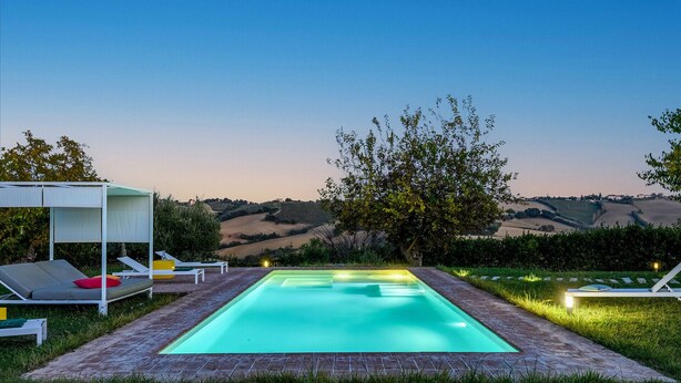 A swimming pool with a view of rolling hills, surrounded by grass and a pergola with lounge chairs. - Villa Traiani 8&2 by Marche Holiday Villas (Piagge)