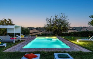 A swimming pool with a view of rolling hills, surrounded by grass and a pergola with lounge chairs. - Villa Traiani 8&2 by Marche Holiday Villas (Piagge)