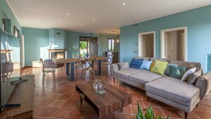 A spacious living room with a large sofa, a dining table, and a fireplace. - Villa Traiani 8&2 by Marche Holiday Villas (Piagge)